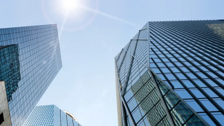 Immeubles de bureaux en verre vus en contre-plongée sous un ciel bleu ensoleillé, symbolisant l'investissement immobilier en SCI