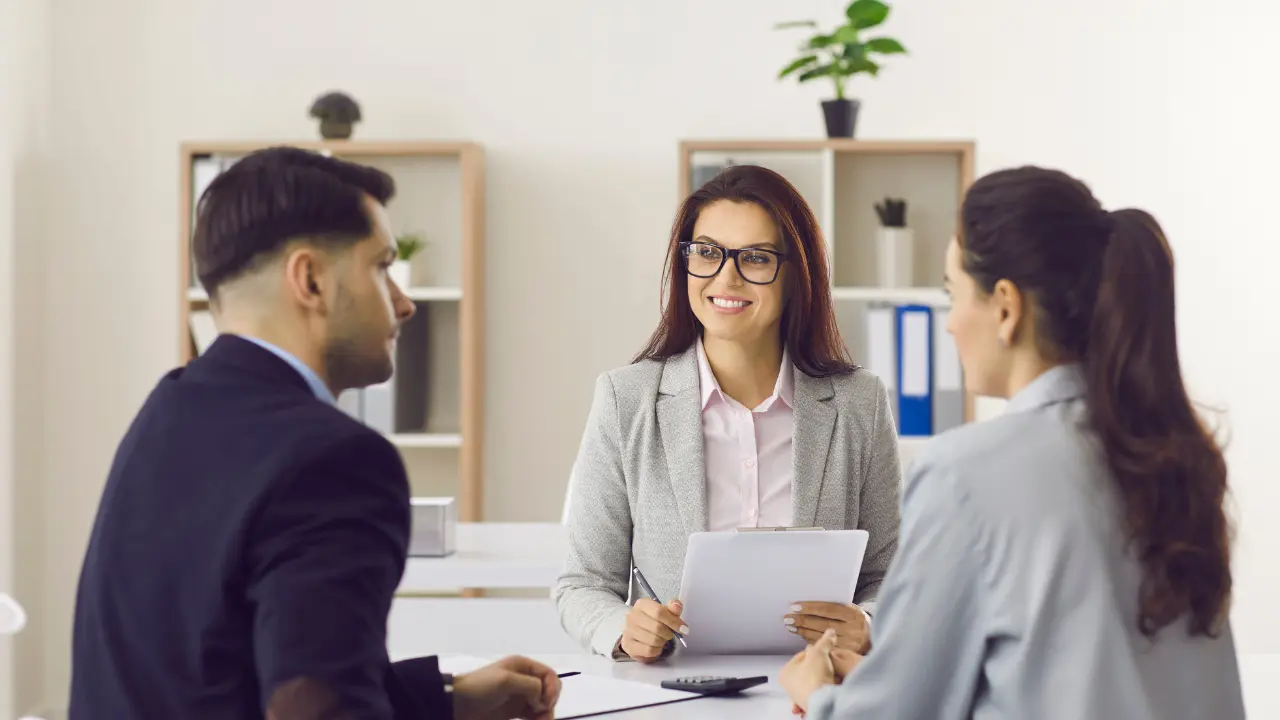 Courtier immobilier conseillant un couple lors d’un rendez-vous de financement, analyse de prêt et accompagnement achat en 2026.