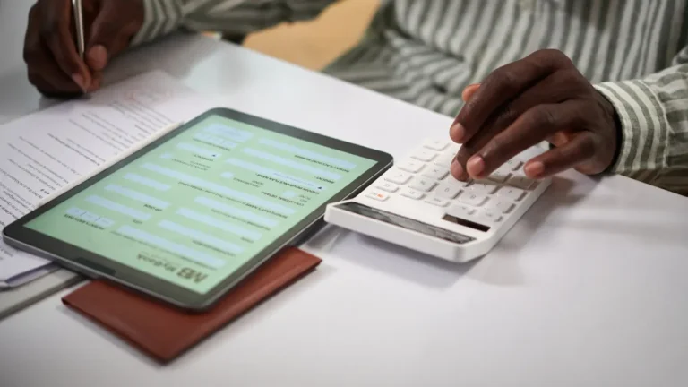 Personne utilisant une calculatrice et une tablette affichant un formulaire bancaire pour simuler un crédit immobilier sans apport.