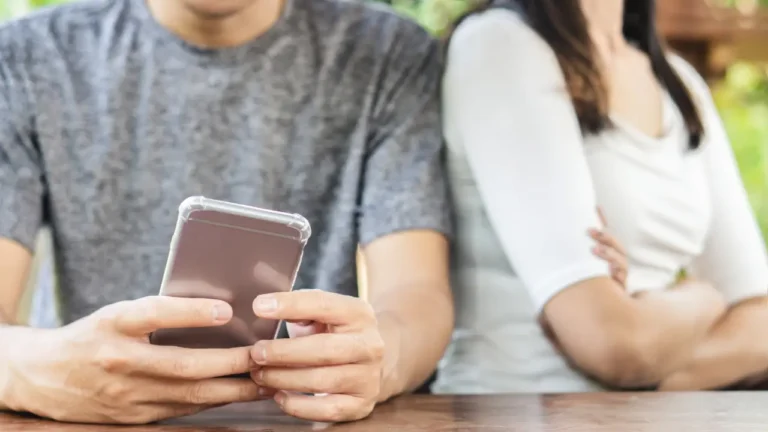 Couple assis dos à dos, l’un consultant son téléphone, illustrant une séparation et les démarches de désolidarisation d’un prêt immobilier en 2026.