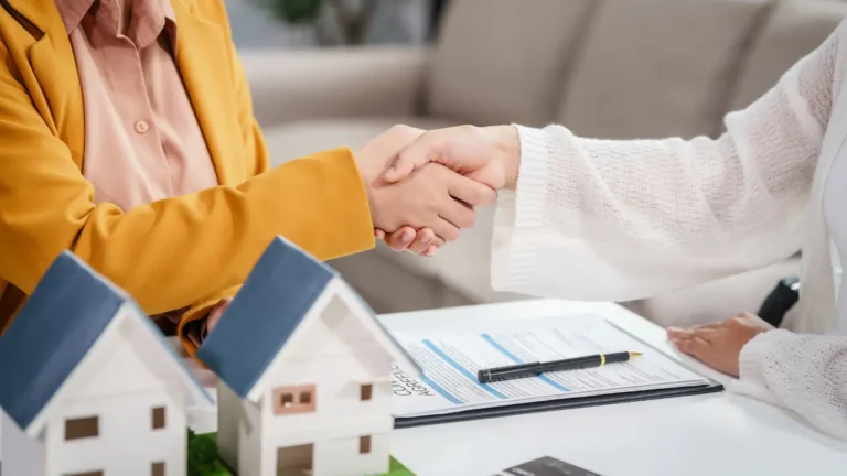 Poignée de main entre un conseiller bancaire et un client après signature d'un contrat de rachat de crédit immobilier, avec maquette de maison sur le bureau.