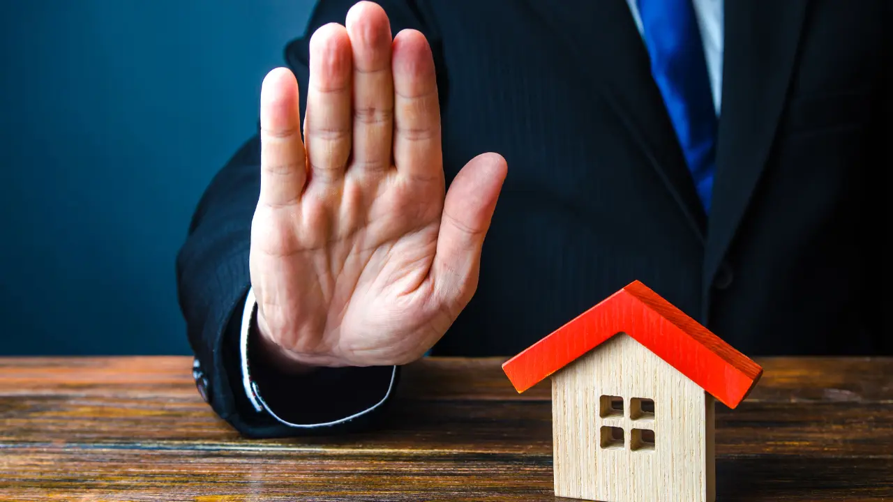 Banquier levant la main devant une maquette de maison illustrant le refus transfert de pret immobilier