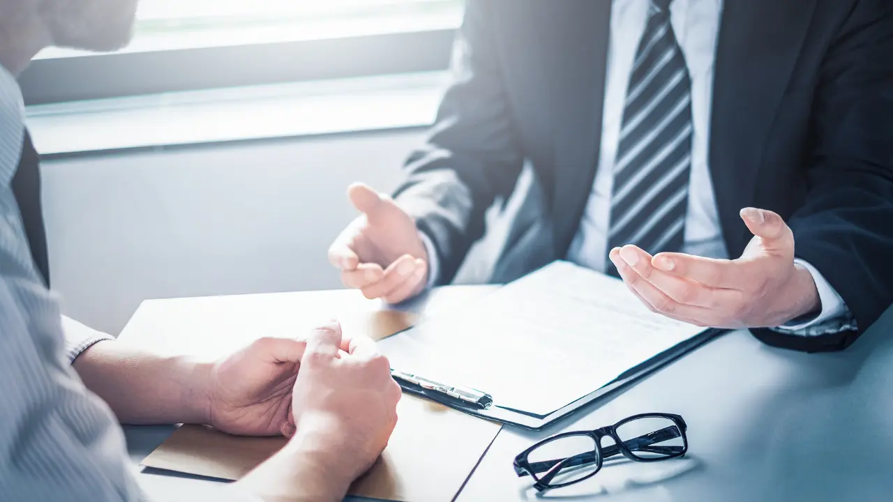 Client en discussion avec son conseiller bancaire pour renégocier son prêt immobilier, documents et lunettes posés sur le bureau.