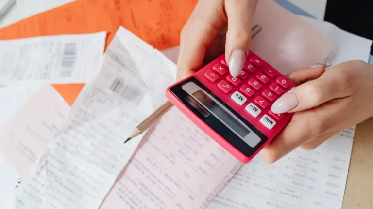 Mains tenant une calculatrice rose au-dessus de documents financiers et factures, illustrant le calcul du taux d'endettement maximum pour un prêt immobilier.